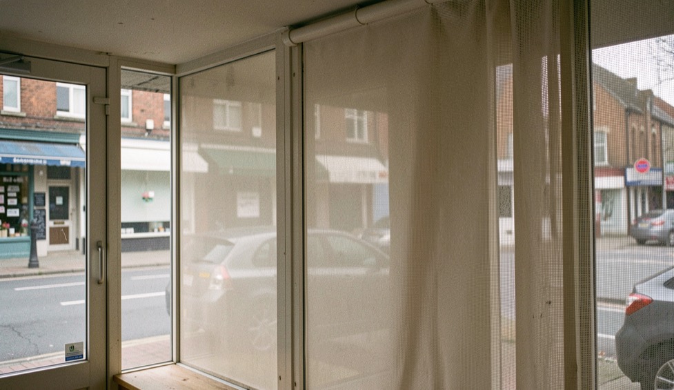 Vitre de boutique couverte d’un film micro-perforé neutre, vue depuis l’intérieur, rue visible en transparence