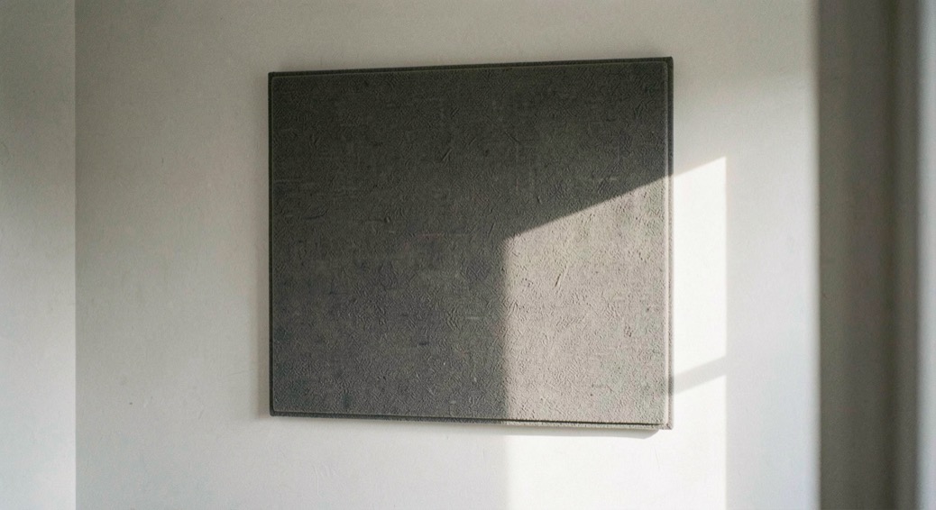 Panneau acoustique textile accroché sur un mur clair d’une salle vide, ombre douce sur le côté